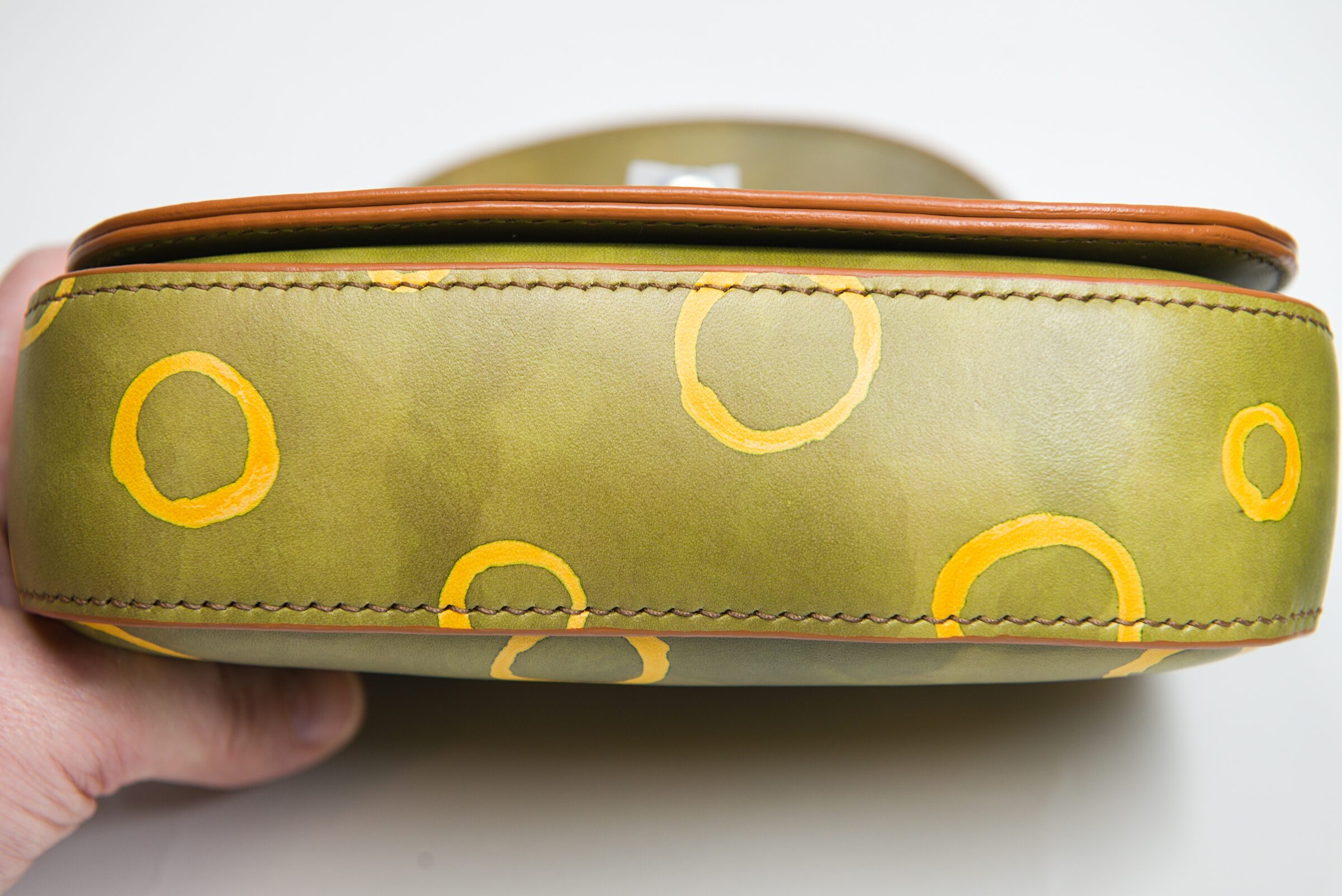 The underside of a sage-green bag held in hand, gold rings wrapping around it