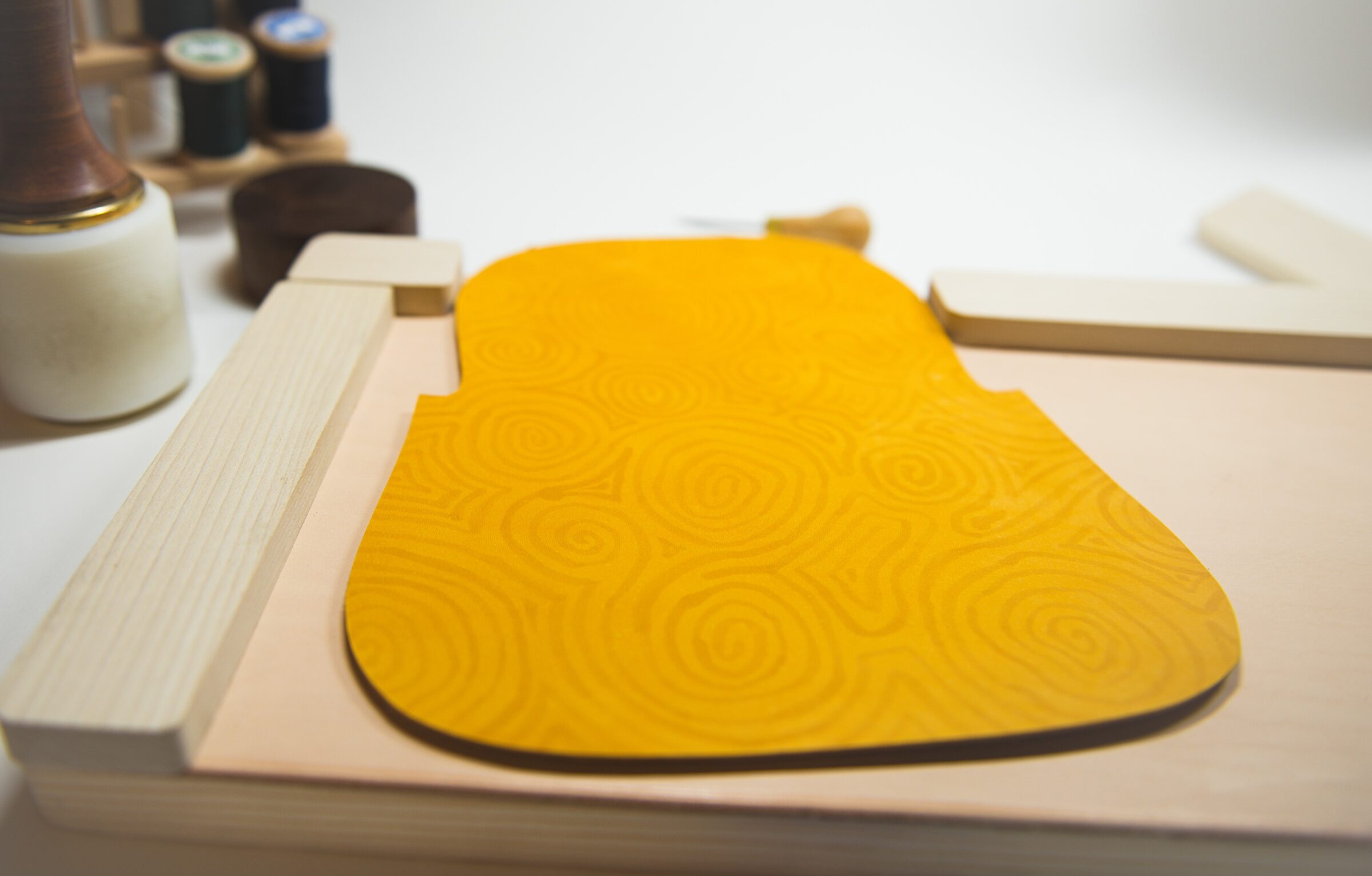 The flap panel, flat and unstitched on the workbench, golden leather covered in brushed swirls